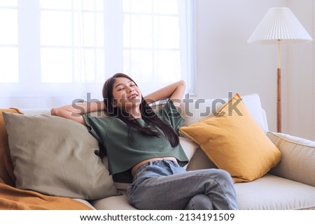 Happy beautiful young asian woman relaxing on sofa at home, enjoying weekend, comfortable in living room dreaming ,relax and chill out concept. Royalty-Free Stock Photo #2134191509