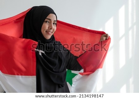 Happy Muslim woman wears black Hijab and Muslim traditional clothes holding irag flag, sunlight and shade on white wall, Muslim woman rights concept