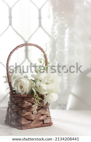 Blurred image of white flowers in a rattan basket on a white wooden table.
