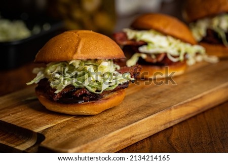 Pork belly sliders on brioche bun with hoisin souse and spicy pickle slaw placed on wood plank