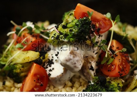 Healthy bowl with bulgur, broccoli, chicken in cream sauce, greens and tomatoes isolated on black background. Healthy food delivery service and daily ration concept. Close-up.