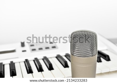 Professional studio microphone for voice and music recording against blurred synthesizer keyboard background with copy space.