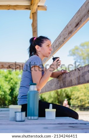young latina woman in the countryside drinking mate. vertical picture