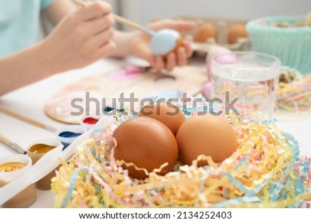 Preparation for Easter. The child is holding a large egg in his hands. Pastel shades on the palette. A child's hand paints an egg light blue with a brush. Happy Easter