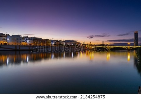 Sunset over the river Guadalquivir in downtown Seville with amazing colors in the sky and a view on the riverside of  the Triana (English Triana) neighbourhood and the illuminated golder tower