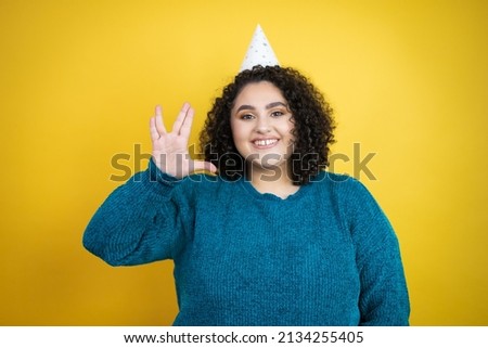 Young beautiful woman wearing a birthday hat over isolated yellow background doing hand symbol