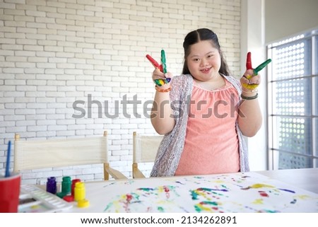 down syndrome teenage girl showing painted hands and doing victory sign, drawing a picture on paper