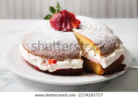 Homemade Victoria sponge cake filled with starwberries, jam and whipped cream decorated with icing sugar and strawberry on a white marble table Royalty-Free Stock Photo #2134265757