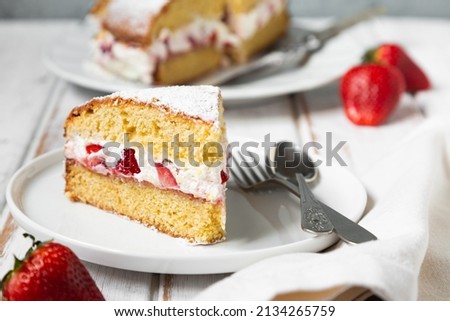 Homemade Victoria sponge cake filled with strawberries, jam and whipped cream decorated with icing sugar and strawberry on a white wooden table 