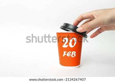 February 20th. Day 20 of month, Calendar date. A woman's hand open black plastic cap of red disposable cardboard  coffee paper cup with Calendar Date. Winter month, day of the year concept