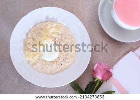 Breakfast in the cafe. A plate of oatmeal porridge on a light background. Greeting card and pink rose on a light background. An empty space for the inscription on the postcard. Top view .Flat lay.