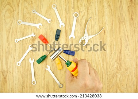 Man holding hammer over of wrench and small screwdriver use for minor repair on wood background. Construction and repair concept photography.