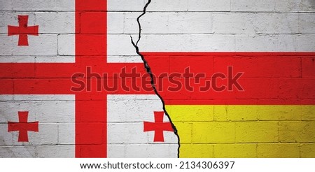 Cracked brick wall painted with a flag of Georgia on the left and a flag of South Ossetia on the right. Royalty-Free Stock Photo #2134306397