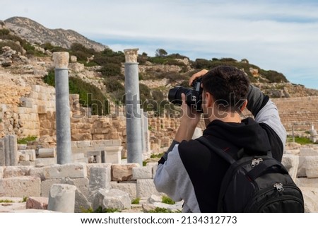 Back view of young traveler tourist boy. He is taking photograph of historical columns in Knidos ancient city. It was a Greek city in ancient Caria, located by sea Datca, Mugla, Turkey.