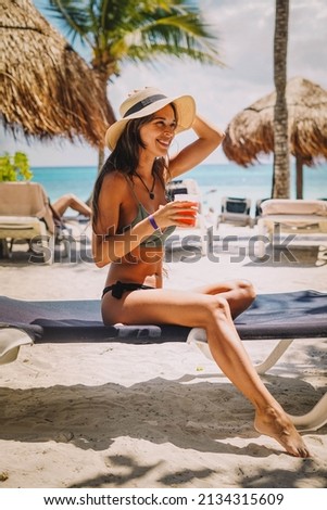 Woman posing in a bikini with a cocktail on a tropical beach
