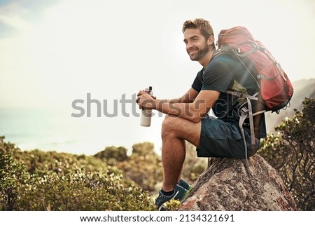 The perfect day to be out in nature.... Shot of a young man taking a water break while out hiking. Royalty-Free Stock Photo #2134321691