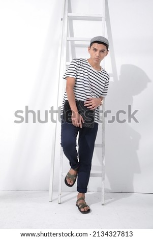 Young man in summer clothes with hat holding handbag with white wooden stairs in studio

