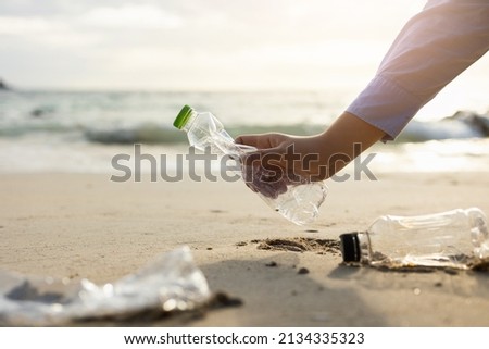 Close up woman hand pick up the plastic bottle on the beach. Female Volunteer clean the trash on the beach make the sea beautiful. World environment day concept. Royalty-Free Stock Photo #2134335323