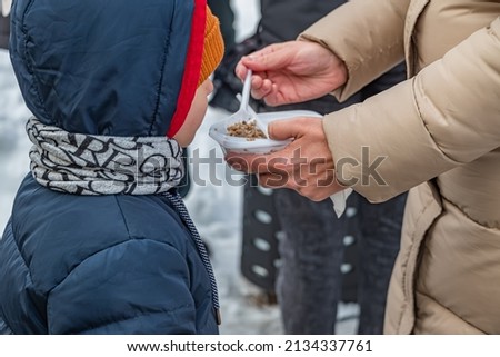 homeless child refugee eats hot food on the street aftermath of war fighting. Royalty-Free Stock Photo #2134337761