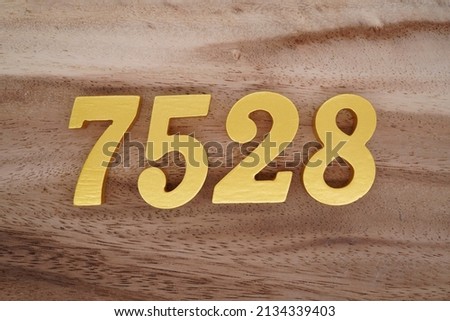 Wooden  numerals 7528 painted in gold on a dark brown and white patterned plank background.