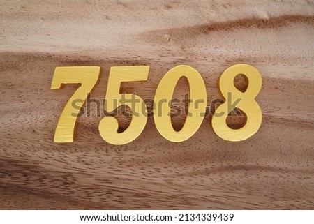 Wooden  numerals 7508 painted in gold on a dark brown and white patterned plank background.