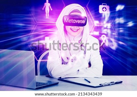 Muslim female doctor wearing VR goggles with metaverse word while working in the cyberspace