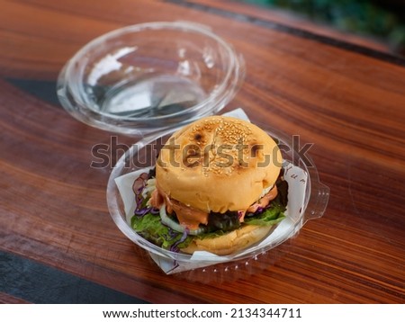 Closeup shot of take away delicious tasty yummy homemade juicy patty grilled beef cheeseburger with vegetable and melting thousand island sauce in disposable plastic round box package on wood table. Royalty-Free Stock Photo #2134344711