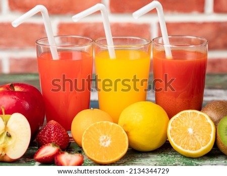 Different fruits juice in glass, apple, orange and strawberry juice with straw, looking refreshing on colourful wood board in front of brick wall background. Picture decorating with fresh fruits.
