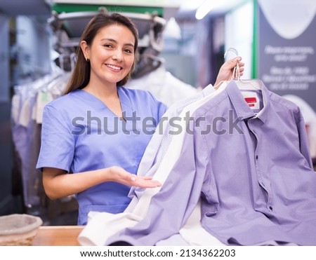 Cheerful woman laundry worker returning clean clothes to customer at dry-cleaning facility Royalty-Free Stock Photo #2134362203