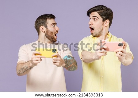 Young shocked fun gambling men friends together in t-shirt play racing games mobile cell phone gadget smartphone isolated on purple background. People lifestyle friendship concept Tattoo translate fun