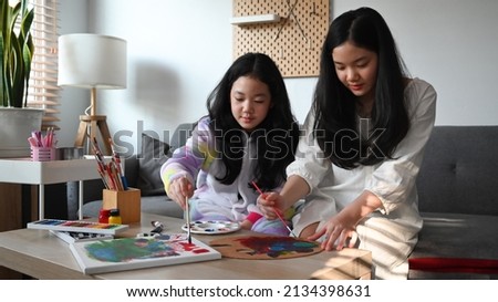 Two cute little sisters enjoy painting picture at home while spending leisure time together.