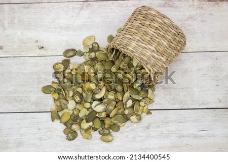 Peeled pumpkin seeds poured from inverted wicker basket on to wooden background