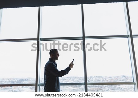 Young business man holding a phone. In an office or business center against the background of large windows of a skyscraper. Work and career, concept