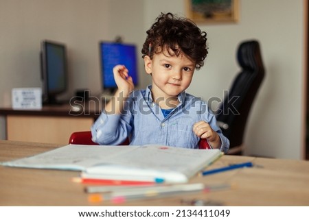 A preschooler learns online at the computer and writes an assignment in a notebook at home. Home online learning