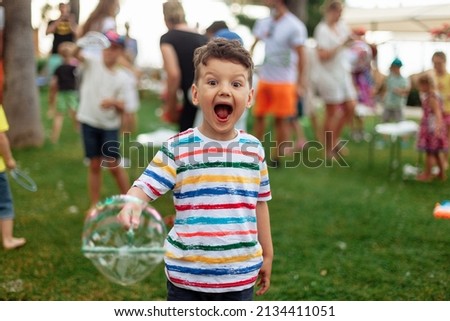 An emotional boy with a big bubble. Summer weekend, recreation, children's animation in the park in the fresh air, animation program with soap bubbles.