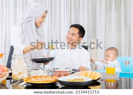 Muslim woman serving foods to her husband and daughter in dining room while having dinner during Eid Mubarak at home Royalty-Free Stock Photo #2134411713