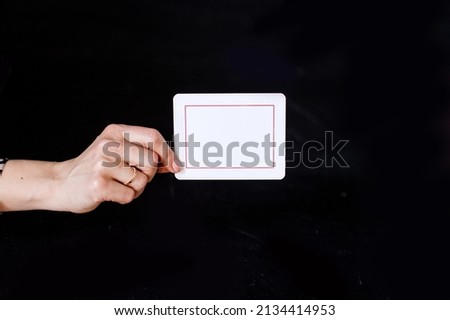 In the female hand there is a white card, inside the card there is a red frame and a text box. Black background of the picture