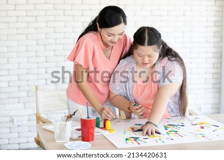 woman teacher and down syndrome girl with painted hands, drawing a picture on paper