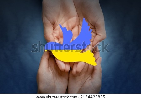 Female hands with paper dove in colors of Ukrainian flag on dark background. Stop the war