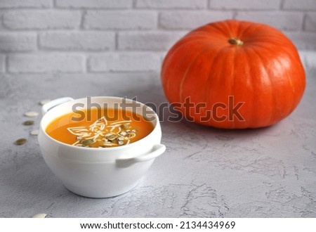 pumpkin soup with pumpkin seeds in a white bowl on a gray background