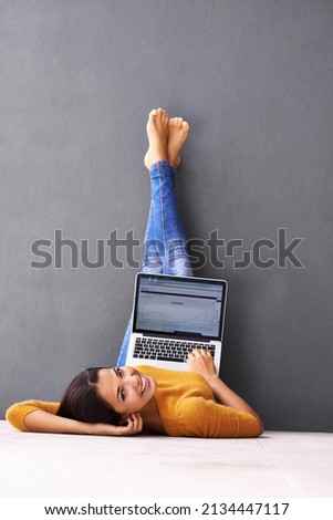 The up-side of technology. A young woman lying on the floor with her laptop against a gray background. Royalty-Free Stock Photo #2134447117
