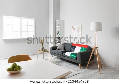 Interior of light living room with black sofa, dining table and UAE flags