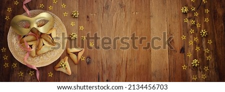 Purim celebration concept (jewish carnival holiday). Hamantaschen cookies and gold carnival mask over wooden background