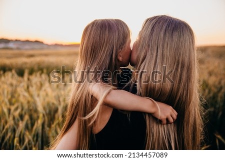 Happy mom and little daughter hugging in field on golden sunset. Summertime