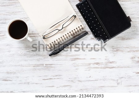 Top view office desk with white cup of coffee. Flat lay vintage wooden table with spiral notebook, pen and organizer. Coffee break time at work. Corporate business concept with copy space.