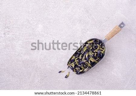 Dry blue flowers in a metal scoop on a light background. Traditional Thai tea. Top view.