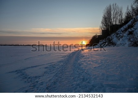 snowy path on the frozen bank of the river. The trail goes into sunset. Photo taken in cases of setting sun