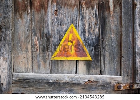 Old high voltage sign. Yellow triangle on a  rusty door. 