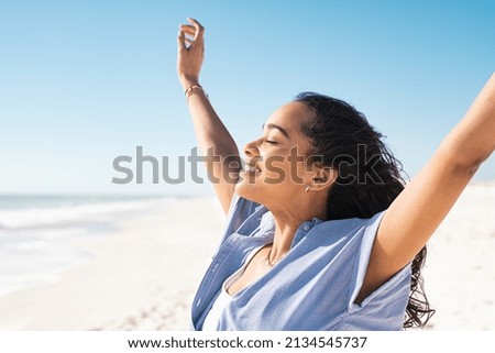 Smiling latin hispanic woman stretching hand and relaxing on beach. Woman breathing deeply at seaside with eyes closed. Happy woman standing on the beach and enjoy the sun tan with arms outstretched. Royalty-Free Stock Photo #2134545737