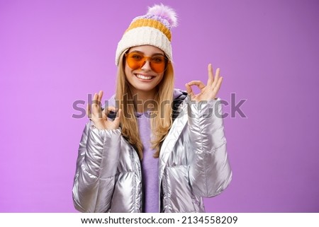 Everything fine thanks. Charming flirty blond confident woman in silver stylish jacket sunglasses winter hat show okay no problem ok gesture smiling affirmative, liking awesome day purple background